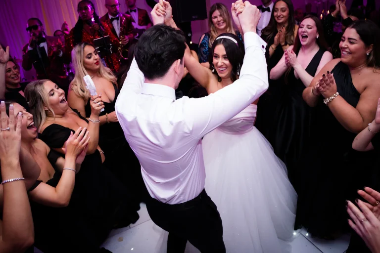 People dancing at a wedding reception. The Groom is holding the Brides hands up.